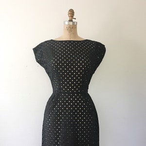 May include: A black sleeveless dress with a round neckline and a dotted pattern. The dress is made of a lightweight fabric and has a fitted silhouette.