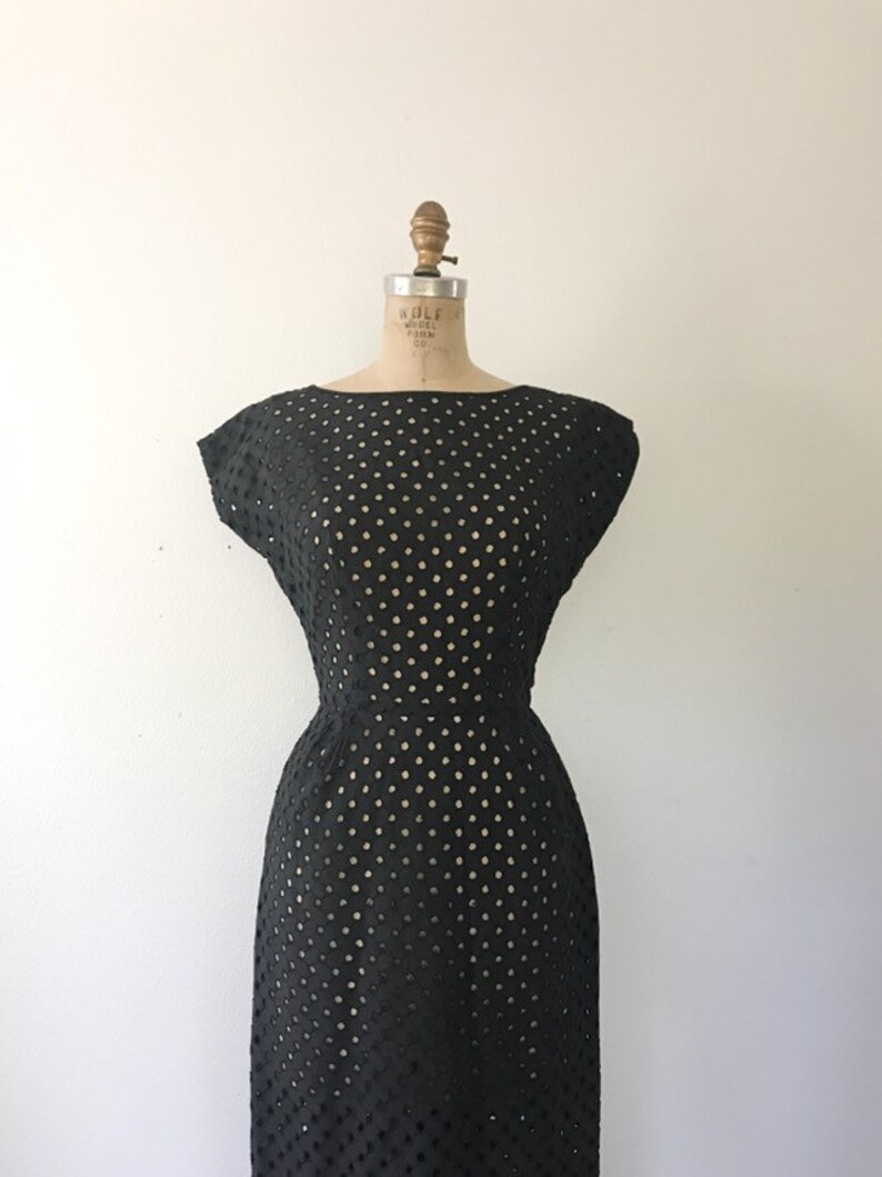 May include: A black sleeveless dress with a round neckline and a dotted pattern. The dress is made of a lightweight fabric and has a fitted silhouette.