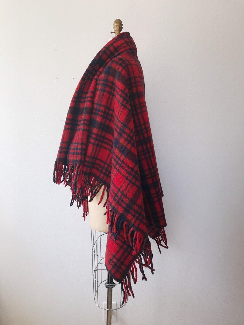 May include: Red and black plaid wool shawl with fringe trim. The shawl is draped over a mannequin.