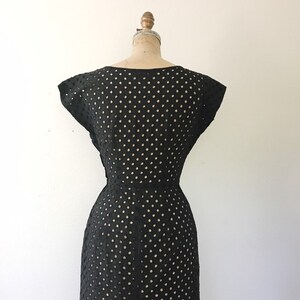 May include: Black sleeveless dress with a polka dot pattern. The dress is made of a lightweight, breathable fabric and has a fitted silhouette.