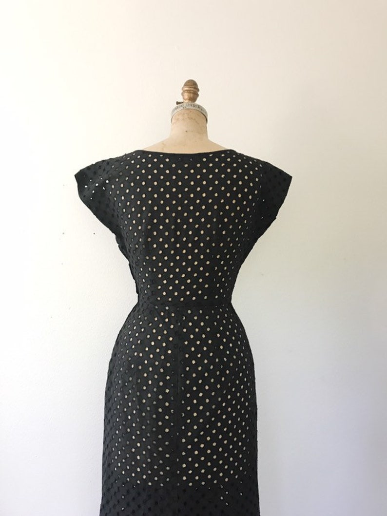 May include: Black sleeveless dress with a polka dot pattern. The dress is made of a lightweight, breathable fabric and has a fitted silhouette.