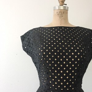 May include: A black dress with a polka dot pattern. The dress is made of a lightweight fabric with a delicate, openwork design. The dress has a fitted bodice and a full skirt.