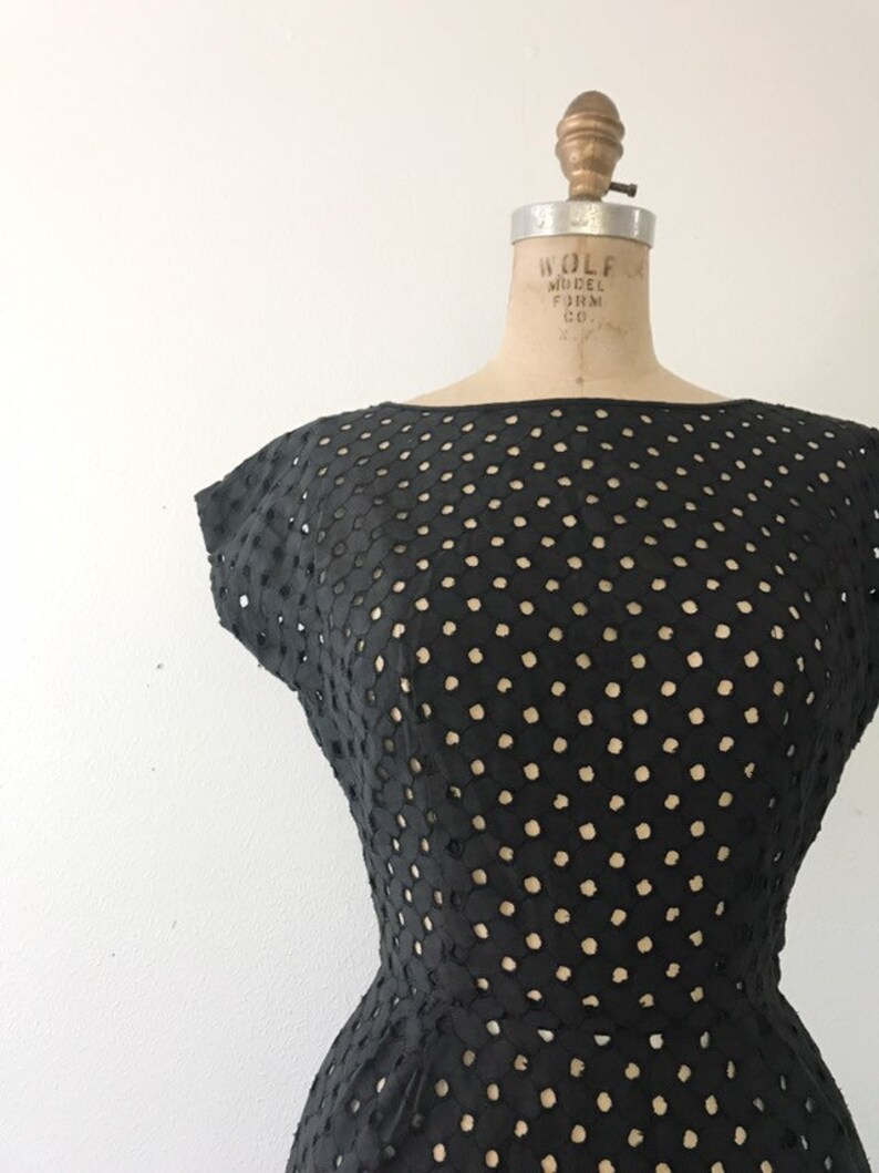May include: A black dress with a polka dot pattern. The dress is made of a lightweight fabric with a delicate, openwork design. The dress has a fitted bodice and a full skirt.