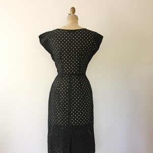 May include: Black dress with a polka dot pattern and a fitted silhouette. The dress has short sleeves and a scoop neckline.