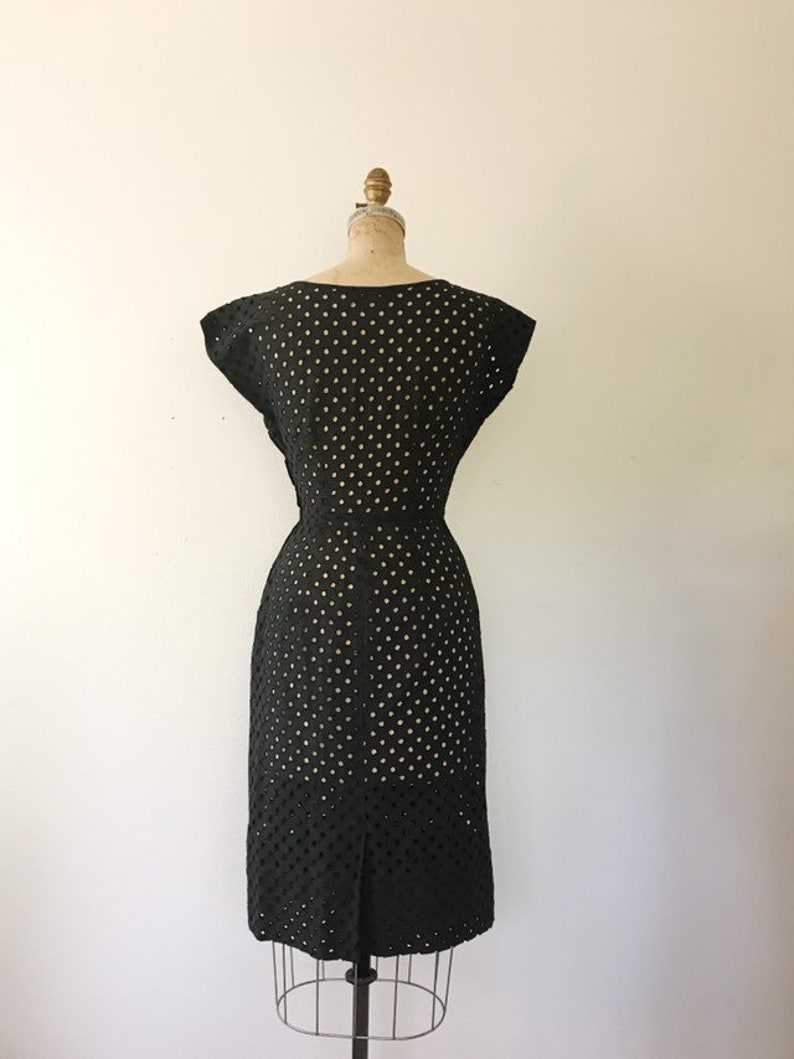 May include: Black dress with a polka dot pattern and a fitted silhouette. The dress has short sleeves and a scoop neckline.