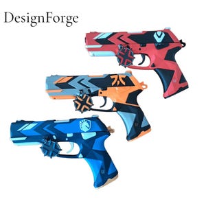 May include: Three toy pistols in red, orange, and blue with geometric designs. The red pistol has black accents, the orange has gray and black, and the blue has white. Each pistol has a circular emblem attached to the side.