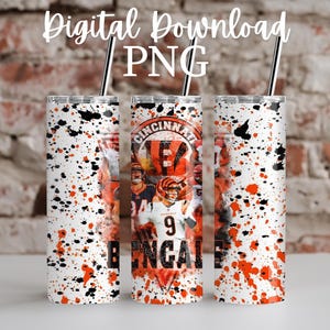 May include: Three white tumblers with black and orange splatter paint design. The center tumbler features a graphic of Cincinnati Bengals players with the text "Cincinnati Bengals".