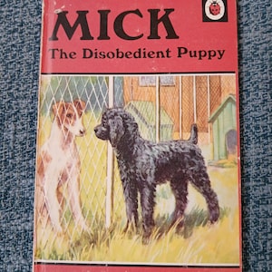 May include: A red book titled "Mick The Disobedient Puppy" with a ladybug logo. The cover shows a black poodle and a white terrier looking at each other through a wire fence.