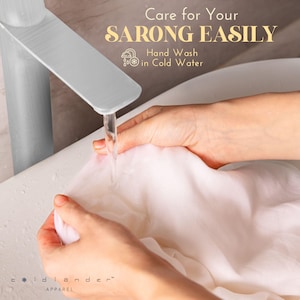 Pu&ograve; includere: Si vedono delle mani che lavano un sarong bianco in un lavandino con acqua corrente. Il testo "Care for Your SARONG EASILY" &egrave; visualizzato sopra il lavandino. Il testo "Hand Wash in Cold Water" &egrave; visualizzato sotto il lavandino.