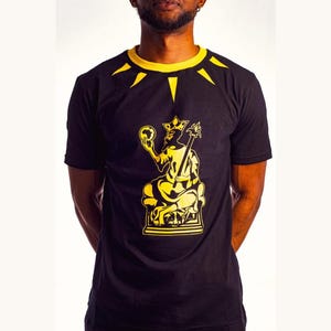May include: Black t-shirt with a gold graphic of a king sitting on a throne holding a globe. The king is wearing a crown and has a beard. The t-shirt has a gold collar with a black and gold pattern.