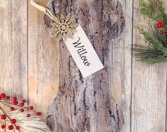 May include: A gray and brown faux fur bone-shaped Christmas stocking with a white tag that says "Willow" and a gold snowflake ornament.