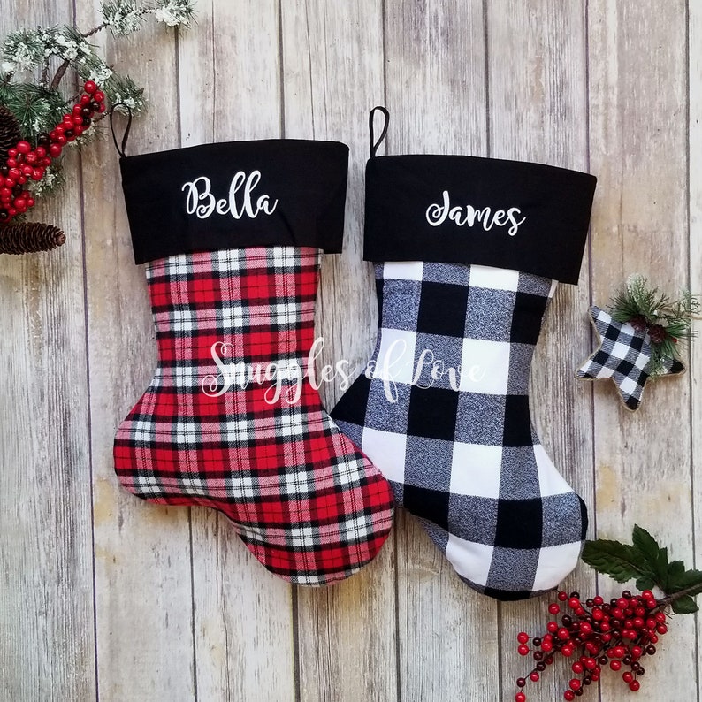 May include: Two personalized Christmas stockings, one red and black plaid with the name "Bella" and one black and white buffalo plaid with the name "James".