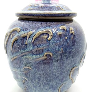 May include: A blue ceramic jar with a lid. The jar has a round shape and is decorated with raised, wave-like patterns in a lighter color. The jar is approximately 6 inches tall.