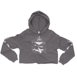 May include: A charcoal grey cropped hoodie with a white graphic of a whale inside a geometric shape with stars and a crescent moon. The sleeves have a white whale graphic.