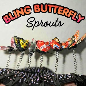 Op de afbeelding: Een set haarclips met kleurrijke vlinderornamenten bevestigd aan dunne metalen veertjes. De vlinders zijn versierd met kleine fonkelende strass-steentjes. De tekst BLING BUTTERFLY Sprouts wordt weergegeven in grote, dikgedrukte, oranje en zwarte letters.