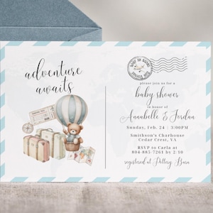 Puede incluir: Una invitación a un baby shower con temática de viaje. La invitación presenta un globo aerostático, un oso de peluche, maletas y las palabras "adventure awaits". La invitación es azul claro con un sobre azul.