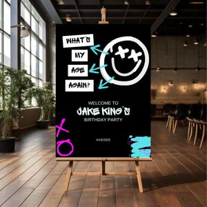 May include: A black and white birthday party sign with the text "What's my age again?" and a smiley face with an X over each eye. The text "Welcome to Jake King's Birthday Party" is below the smiley face. The date "4/16/2025" is at the bottom of the sign.