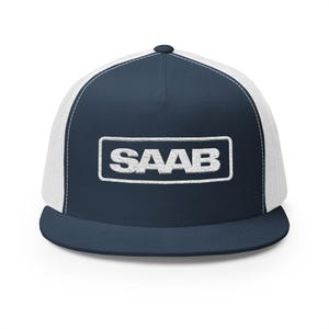 May include: A navy blue and white trucker hat featuring a structured front panel with the word SAAB embroidered in white inside a rectangular border. The cap has a flat brim, a navy blue crown, and white mesh side and back panels for ventilation.