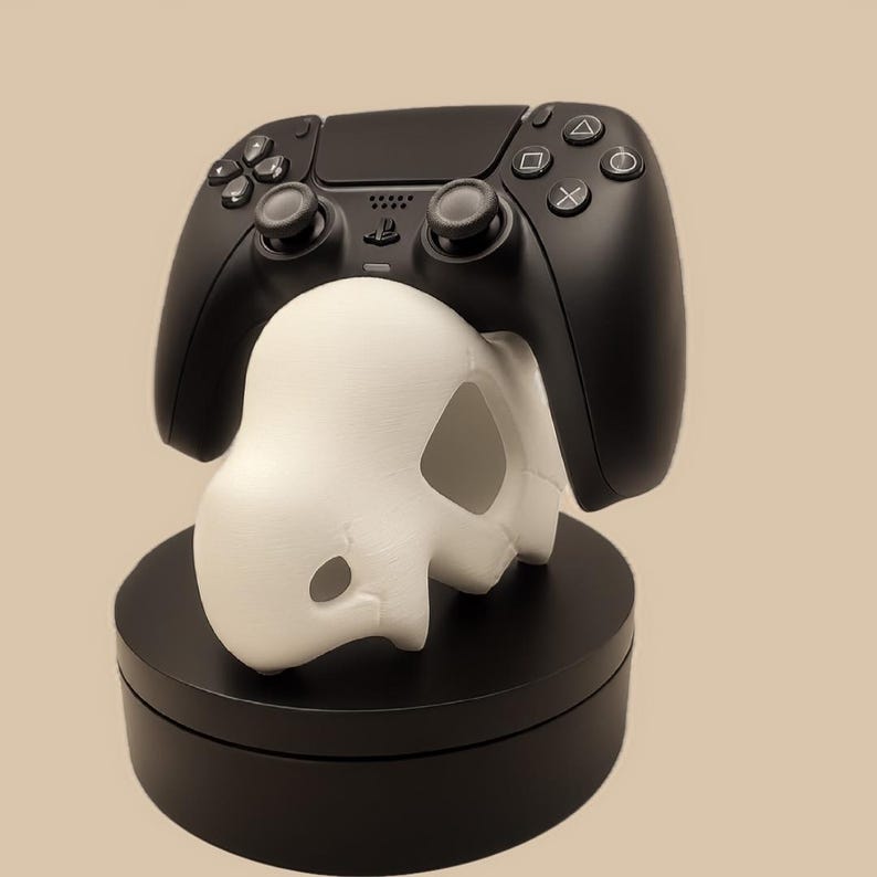 Puede incluir: Un mando de videojuegos inal&aacute;mbrico negro descansa sobre un soporte blanco con forma de dinosaurio estilizado. El soporte est&aacute; colocado sobre una base negra circular. El mando cuenta con botones direccionales est&aacute;ndar, dos joysticks y el logotipo de PlayStation.