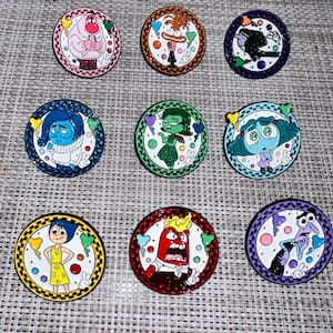 May include: Nine round enamel pins featuring characters from the animated film Inside Out. Each pin depicts a different emotion: Joy, Sadness, Anger, Fear, Disgust, Bing Bong,  and  the  characters  from  the  film  'Inside  Out'.