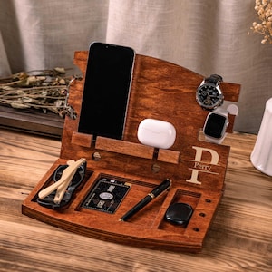 May include: A wooden desk organiser in a rich brown finish. It features slots for a smartphone, wireless earbuds, a watch, and a smart watch. There are also compartments for glasses, a pen, a credit card, and a small black item. The organiser is personalised with the name "Perry".