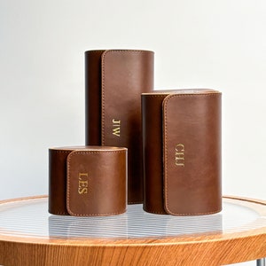 Può includere: Tre custodie per rotoli di orologi in pelle marrone con lettere dorate. Le custodie sono monogramma con le iniziali "LES", "CHJ" e "J.W."