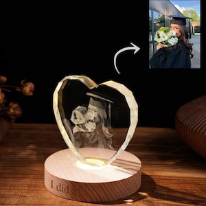 Pode incluir: Foto de cristal em forma de coração com tema de formatura, iluminada em uma base de madeira. O cristal apresenta uma imagem 3D de uma graduada segurando flores. A base é gravada com as palavras "I did it!"