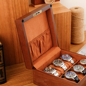Puede incluir: Una caja de madera rectangular para relojes con tapa abatible y cierre de color lat&oacute;n. El interior est&aacute; forrado con tela suave de color tostado, con un bolsillo fruncido en la tapa y cinco ranuras acolchadas para relojes plateados.
