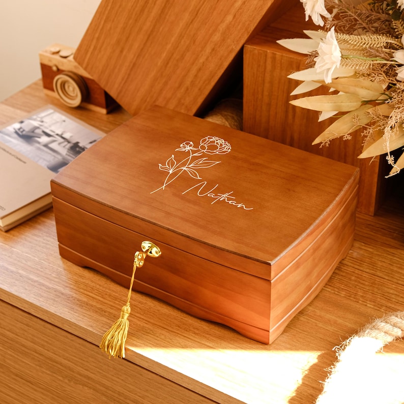 May include: A wooden jewelry box with a floral design and the name "Nathan" engraved on the lid. The box has a gold latch and a tassel.
