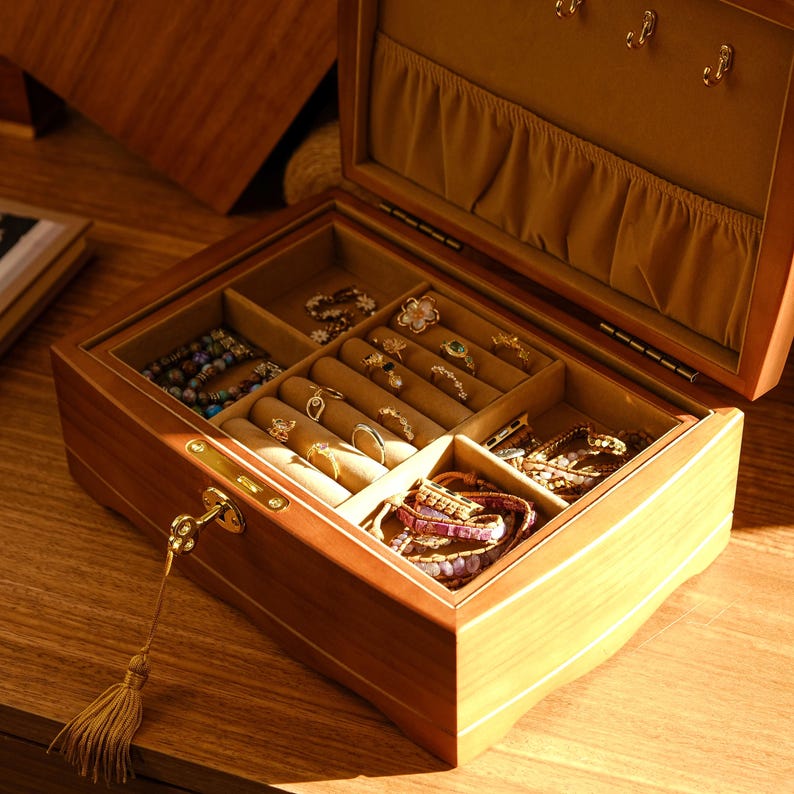 May include: A wooden jewelry box with a key lock and multiple compartments for storing rings, bracelets, and necklaces. The box is open and the interior is lined with brown velvet.