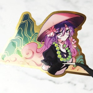 May include: A gold-edged sticker featuring an anime-style character with purple hair and a pink hat. The character wears a black outfit and a green beaded necklace. The background includes a mountain range and clouds.