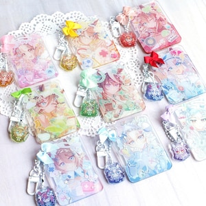 May include: A collection of eight rectangular acrylic keychains featuring colorful anime-style character illustrations. Each keychain includes a small matching ribbon bow, a silver-toned metal lobster clasp, and a secondary miniature acrylic charm.