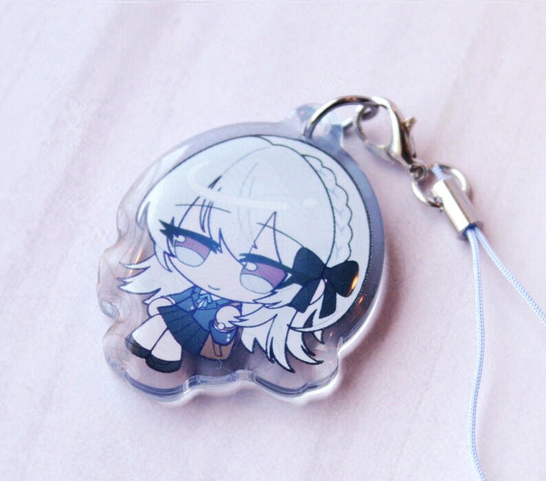 May include: A clear acrylic charm featuring a chibi-style illustration of a character with white hair, a black hair bow, and a blue school uniform. The charm is attached to a silver-toned metal lobster clasp and a thin, light blue cord strap.