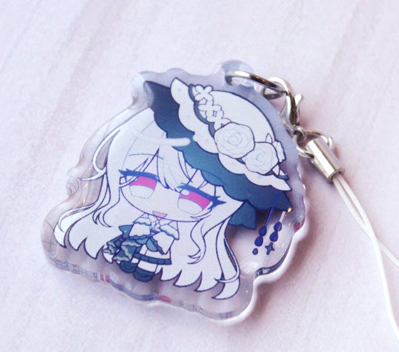 May include: A clear acrylic charm featuring a stylized anime character with long white hair, wearing a white hat adorned with roses and a dark blue brim. The character has pink eyes and a white outfit with dark blue accents, attached to a silver clasp.