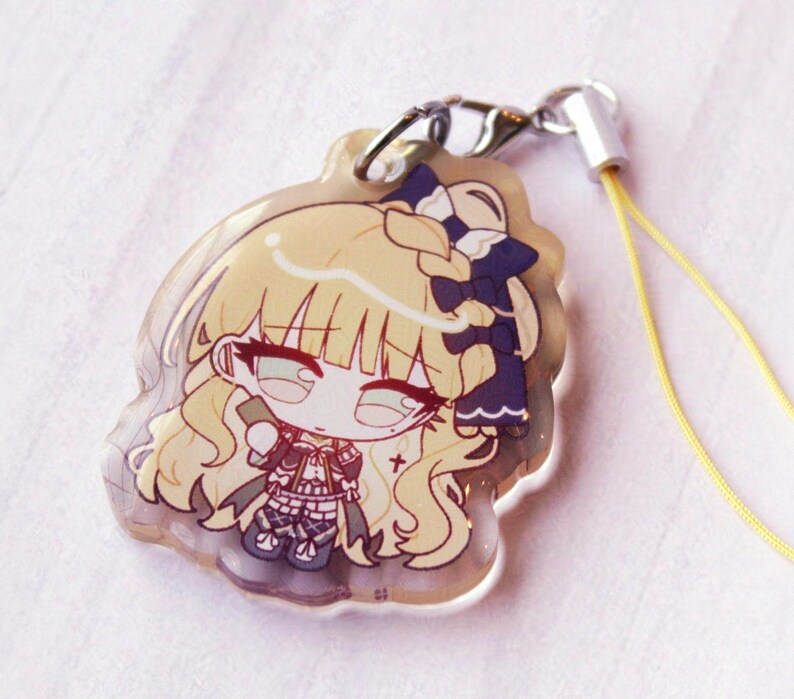 May include: A clear acrylic charm featuring a chibi-style illustration of a character with long blonde hair, a dark blue bow, and a detailed outfit. The charm includes a silver metal lobster clasp and a thin yellow cord for attachment.