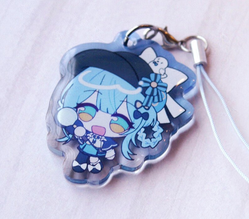 May include: A clear acrylic charm featuring a chibi-style character with light blue hair, wearing a dark blue hat and outfit with white accents. The character has large teal eyes and is holding a small white object. A silver lobster clasp is attached.