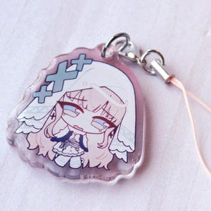 May include: A clear acrylic charm featuring a stylized illustration of a character with long light hair wearing a white veil and a dress. The design includes three blue cross symbols and is attached to a silver metal lobster clasp with a light pink cord.