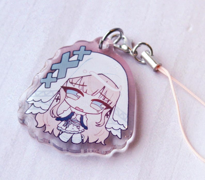 May include: A clear acrylic charm featuring a stylized illustration of a character with long light hair wearing a white veil and a dress. The design includes three blue cross symbols and is attached to a silver metal lobster clasp with a light pink cord.
