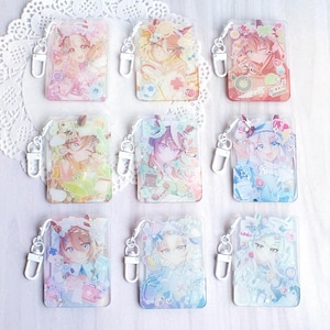 May include: A collection of nine rectangular acrylic keychains featuring anime-style character illustrations in various pastel color palettes. Each keychain includes a silver-toned metal lobster clasp and displays unique decorative elements like flowers, stars, and small objects surrounding the central character portrait.