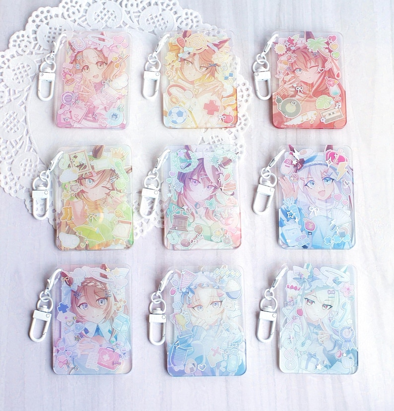 May include: A collection of nine rectangular acrylic keychains featuring anime-style character illustrations in various pastel color palettes. Each keychain includes a silver-toned metal lobster clasp and displays unique decorative elements like flowers, stars, and small objects surrounding the central character portrait.
