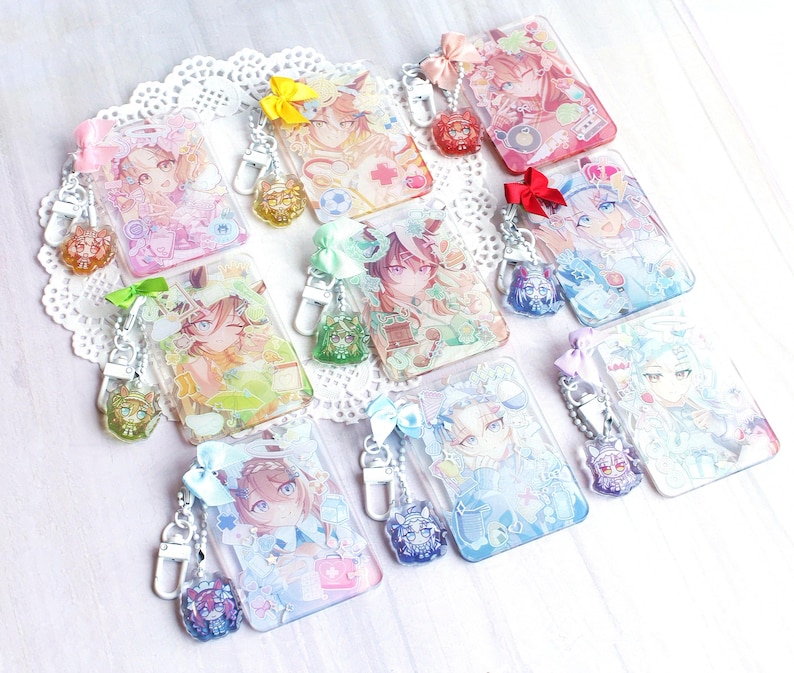 May include: A collection of eight rectangular acrylic keychains featuring colorful anime-style character illustrations. Each keychain includes a small matching ribbon bow, a silver-toned metal lobster clasp, and a secondary miniature acrylic charm.