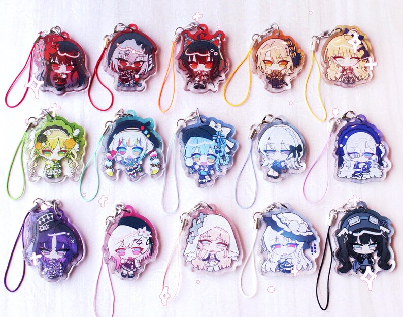 May include: A collection of fifteen acrylic charms featuring diverse anime-style character illustrations. Each charm is attached to a colorful looped cord and displays a unique chibi-style figure with distinct hair colors, outfits, and accessories.