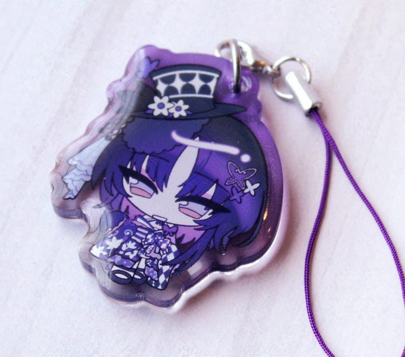 May include: A purple acrylic charm featuring a stylized anime character with dark hair, wearing a top hat with a checkered pattern and floral accents. The character has a purple outfit with a checkered skirt and is attached to a purple cord strap.