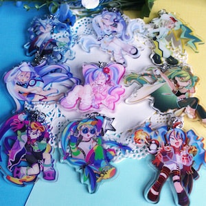 May include: A set of nine colorful anime character acrylic charms. The charms feature different characters with various poses and expressions. The charms are all on a white background.