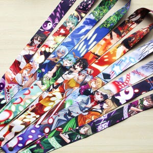 May include: A collection of colorful lanyards featuring anime-style character designs. The lanyards display various patterns and illustrations, including characters, symbols, and abstract designs. Each lanyard is made of a smooth, printed fabric and includes a metal clasp.