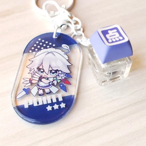 May include: A keychain featuring an oval acrylic charm with a white-haired anime character, the text "POINT" and three stars, attached to a white metal ring and a light purple mechanical keyboard keycap with a white character symbol on top.