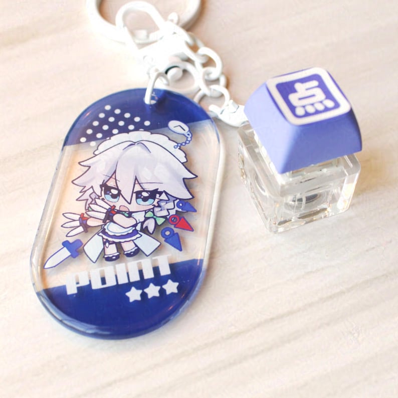 May include: A keychain featuring an oval acrylic charm with a white-haired anime character, the text "POINT" and three stars, attached to a white metal ring and a light purple mechanical keyboard keycap with a white character symbol on top.