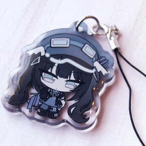 May include: A clear acrylic charm featuring a stylized anime-inspired character with long black hair, wearing a dark blue hat with goggles, a matching outfit, and boots. The charm includes a silver metal jump ring and a thin black cord attachment.