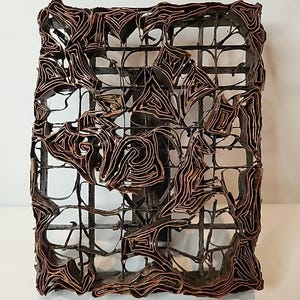 Puede incluir: Una pieza de arte rectangular de metal marrón oscuro con una estructura similar a una rejilla. La pieza presenta intrincados diseños en capas de color cobre que crean un patrón abstracto texturizado. La obra de arte está sobre un fondo blanco.