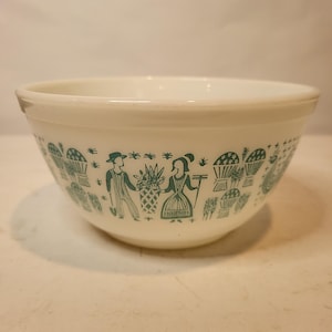 以下が含まれることがあります： 外側にティール色の牧歌的なデザインが施された白いヴィンテージミキシングボウル。デザインは人物、バスケット、花の要素が特徴です。ボウルは丸みを帯びた形状で、滑らかで光沢のある仕上がりです。
